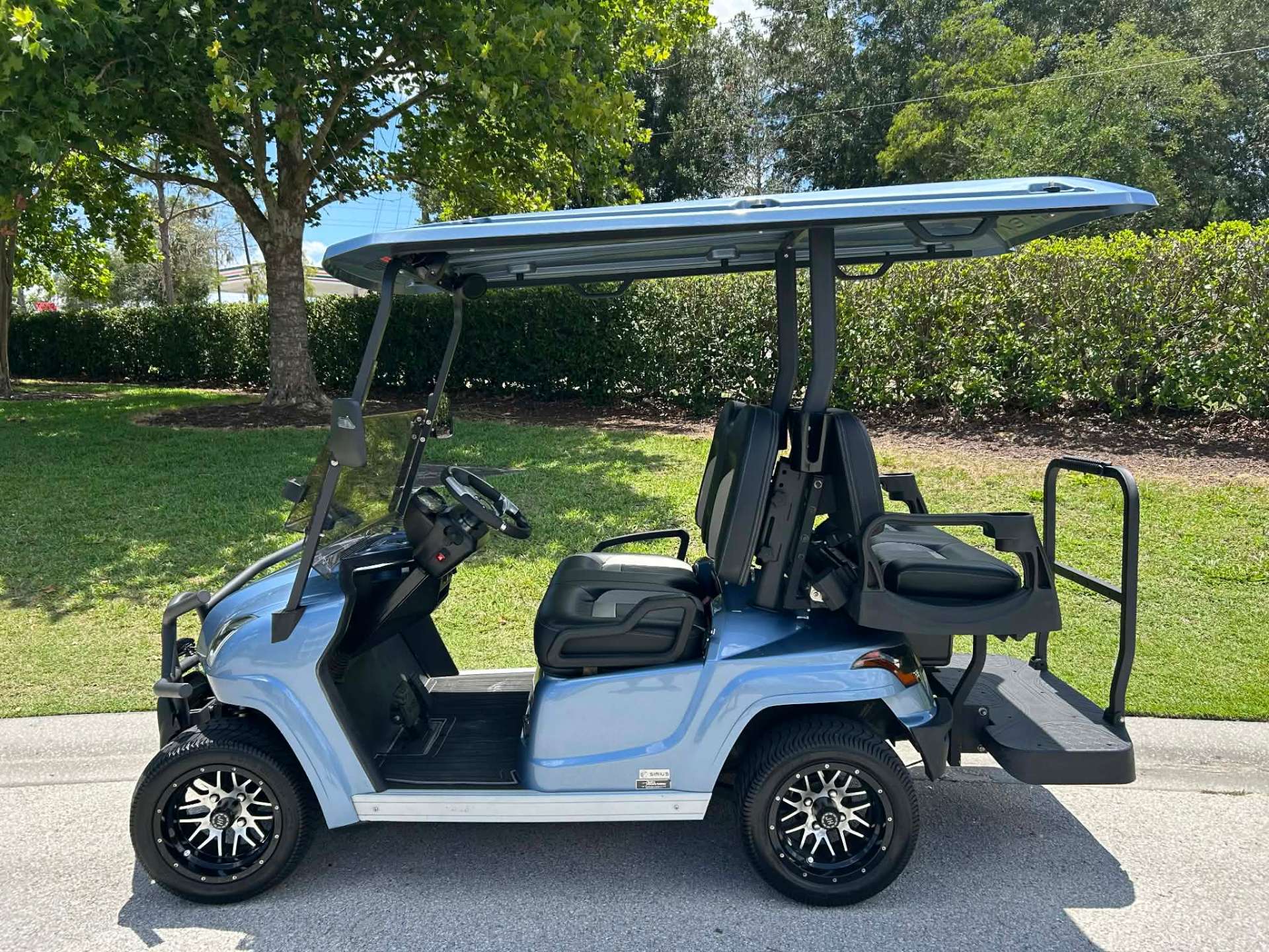 Light blue 4-seater lifted golf cart with rear-facing seat parked on a resort street