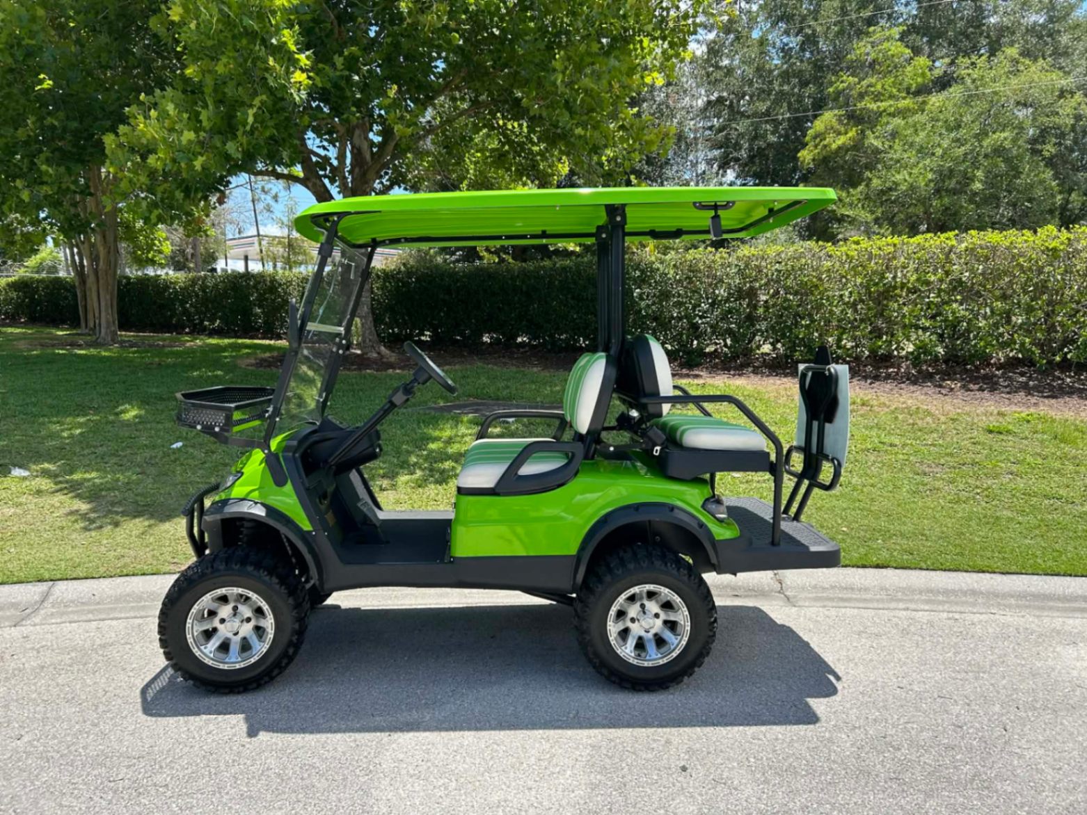 Side view of bright green lifted golf cart with striped seats parked by a resort lawn